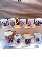Overall view of all eight commemorative mugs and creamers on two shelves with ruler for scale