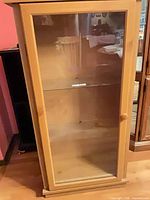 Front view of maple curio cabinet showing glass door, wood knob and interior glass shelf
