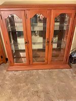 Front view of maple curio cabinet showing three glass doors and plinth base