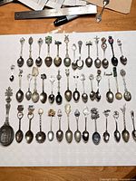 Full layout of approx. 48 souvenir spoons showing variety of designs