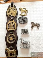 Front view of entire lot showing leather hanger with brass brasses and loose metal horse items