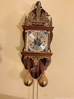 Front view of wooden wall clock with brass crest, painted dial, twin brass weights