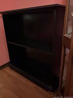 Front view of the black two-shelf bookcase showing overall structure and caster wheels