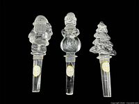 Front view of three clear glass Christmas-themed bottle stoppers