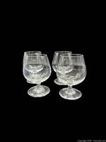 Four clear lead crystal brandy snifter glasses grouped on black background