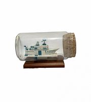 Side view of glass bottle on wooden base showing origami business-card ship inside