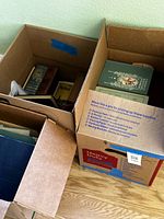 Two boxes with assorted hardcover books, shopping bag partially visible