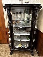 Full view of dark brown curved glass curio cabinet with glass shelves and claw feet