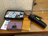 Group shot of flashlight, matchboxes, magnifier, pamphlet, tin and small hardware