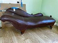Full view of brown leather chaise lounge showing shape and casters