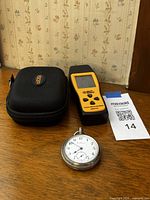 Pocket watch, handheld device and carry case grouped on table