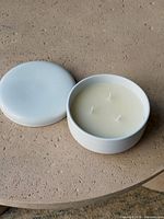 Open ceramic jar showing unused ivory wax and three wicks beside detached lid