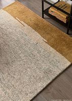 Corner of rug showing cream and ochre color blocks and pile texture beside table