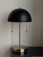 Full view of lamp showing black dome shade, brushed gold stem and base