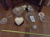 Entire lot laid out showing glass bowls, coasters, porcelain dishes and trinkets with measuring tape for scale