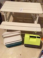 Lot overview showing white plastic picnic table, teal cooler, lime green container