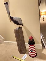 Pelican figurine on wood stump and lighthouse standing beside tape measure