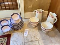 Group view showing stacked blue-rimmed cups & saucers, two red-border pitchers and four bowls