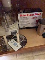 Lot overview showing Cuisinart food processor, KitchenAid grinder box, two discs and milkshake cup
