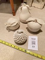 Group view of four white ceramic fruit pieces with ruler for scale
