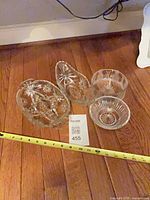 Four clear pressed glass bowls on floor with tape measure for scale