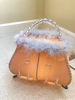 Front view of lit purse-shaped lamp showing feather trim, prisms and bead handle
