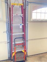 Full view of ladder stored between garage door rails with dolly in front