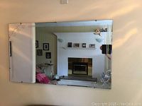 Mirror mounted on wall reflecting room interior with sofa and fireplace, showing etched floral corner detail.