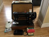 Full view of vintage Singer sewing machine mounted on wooden base with accessory boxes and carrying case behind it.