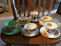 Top view of 6 tea cup and saucer pairs arranged on wooden table showing floral patterns and colors