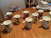 Eight Royal Albert ceramic mugs on wooden table, featuring detailed rose floral patterns in red, pink, and cream colors with gold trim at top and base.