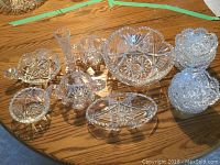 Photo showing the collection of Corinthian pattern crystal glassware including fruit bowl, creamer, sugar bowl, fruit nappies and additional pieces arranged on wooden table.