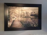 Framed photo of a wooden boardwalk path through marshy area with trees and water, sepia tone, with black frame