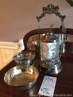 Photo of Victorian pickle jar with detailed silver-plated metalwork and two silver-plated dishes on a wooden surface.