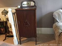 Front angle view of vintage oak sheet music cabinet with door closed, showing decorative carved detail and mirror insert on top.