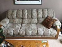 Front view of the upholstered couch showing textured fabric upholstery, wooden armrests and single pillow on right side.