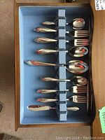 Silver plate flatware arranged in drawer with blue fabric lining, showing spoon and fork handles with Springtime floral pattern