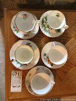 Top down view of 5 tea cup and saucer sets arranged on a wooden table showing different floral patterns and gold trim details