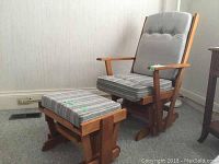 Wood framed glider rocker chair with gray cushioned seat and back, accompanied by matching foot stool with striped cushion on wooden frame.