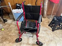 Front view of red transport chair showing seat and wheels