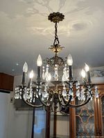 Full view of hanging brass chandelier lit, showing eight arms and crystal drops