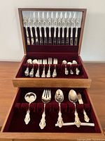 Flatware set in two-tier wooden chest showing knives in lid, assorted forks and spoons in upper drawer, serving pieces in lower drawer