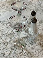 Top view of two floral glass candle holders and two pressed-glass S & P shakers on lace tablecloth