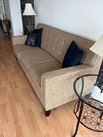 Angled side view highlighting armrest, fabric texture and wooden legs