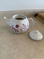 Full view of ceramic teapot showing red floral design and detached lid