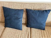 Front view of two matching navy blue square pillows on beige sofa