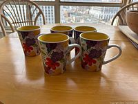 Five floral ceramic mugs on table showing pattern and handles