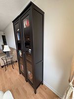 Side view of two tall black glass-door bookcases standing together