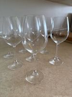Six of the eight clear stemmed wine glasses grouped on countertop