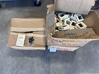 Two cartons containing many small boxed metal bottle openers; one opener and screw bag displayed